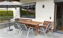 An inviting outdoor area with a wooden table and chairs. A sunshade protects against direct sunlight.