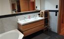 A modern bathroom with a double sink made of wood and elegant fixtures. The walls are light and the floor is made of dark tiles.