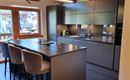 Modern kitchen with dark furniture and a large kitchen island. Large windows let in plenty of daylight and offer a view outside.