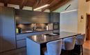 Modern kitchen with a large kitchen island and stylish bar stools. The room has a bright and open atmosphere with wooden ceilings and modern surfaces.
