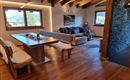 A cozy living kitchen with wooden ceilings and a large dining area. In the background, there is an inviting sitting area with a view of the countryside.