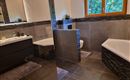 A modern bathroom with an elegant bathtub and a stylish sink. Large windows let in plenty of daylight and offer a view of the green surroundings.