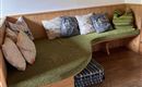 Eine gemütliche Sitzecke mit gepolsterten Kissen und einer grünen Decke. Im Hintergrund hängt ein gemaltes Bild und der Boden ist aus Holz.