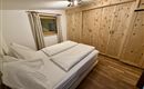 Ein gemütliches Schlafzimmer mit einem Doppelbett und Holzschränken. Große Fenster sorgen für Licht und eine helle Atmosphäre.