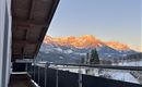 A terrace overlooking snow-capped mountains at sunset. The sky is clear and radiates in soft colors.