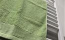 Een groene handdoek ligt op een witte handdoekhouder. De achtergrond is licht en modern ingericht.