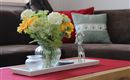 A stylishly decorated table with a flower vase and a small decorative object. In the background, a cozy sofa and cushions can be seen.