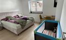 Een moderne slaapkamer met een groot bed en een gezellige deken. In de hoek staat een kinderbed en een klein bureau.
