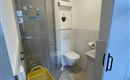 Een moderne badkamer met een doorzichtige douche en een toilet. Gele opbergmanden staan in de ruimte.