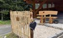 A beautiful entrance area with a wooden railing and a wooden bench. The ground is covered with pebbles and there is a lot of greenery in the surroundings.