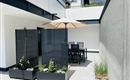 A modern terrace with a dining table and a sunshade.  
Surrounded by decorative plants and a well-kept wall.