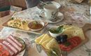 Ein gedeckter Tisch mit verschiedenen Frühstücksleckereien. Darauf sind Käse, Schinken, Tomaten und eine Tasse Kaffee zu sehen.