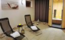 Ein entspannender Wellnessbereich mit zwei Liegen und sanfter Beleuchtung. Im Hintergrund ist eine Sauna zu sehen, die zur Ruhe und Erholung einlädt.