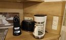 Een moderne keukenoek met een koffiemachine, een broodrooster en een espressomachine. Het meubilair is van licht hout en creëert een uitnodigende sfeer.