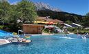 Ein schöner Pool mit klarem Wasser und einer sonnigen Umgebung. Im Hintergrund sind Berge und Grünflächen zu sehen.