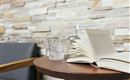 Een Open boek ligt op een ronde houten tafel. Naast het boek staan een glas water en een kan, voor een mooie stenen muur.