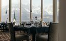 Een elegant restaurant met uitzicht op besneeuwde bergen. De tafels zijn smaakvol gedekt en grote ramen laten veel licht binnen.