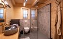 Een moderne badkamer met houten panelen en een grote glazen douche. De wastafel is stijlvol en rond, en er zijn ramen die voor natuurlijk licht zorgen.