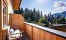 Een houten balkon met een gezellige zithoek. Op de achtergrond zijn groene bossen en bergen te zien.