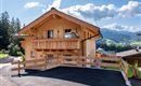 Een traditioneel chalet van hout in een schilderachtige berglandschap. De omgeving is groen met mooie bergen op de achtergrond.