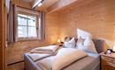 Een gezellig slaapkamer met houten wandpanelen en een groot bed. Er zijn kussens en een kleine nachttafel lamp naast het bed.