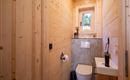 Een kleine badkamer met houten wandbekleding en ramen. Het bevat een toilet en een modern wastafel.