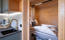 Een gezellige houten kamer met een bed en een moderne keukenhoek. Het licht is warm en creëert een uitnodigende sfeer.