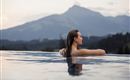 Een vrouw ontspant in een infinitypool met uitzicht op de bergen. De zachte avondstemming en het rustige landschap creëren een ontspannende sfeer.