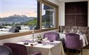 An elegant restaurant with purple chairs and table decoration. In the background, majestic mountains and a beautiful sky are visible.