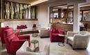 A cozy lounge area with red and beige armchairs.  
Large windows and stylish decorations create an inviting atmosphere.