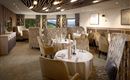 An elegant restaurant with cozy tables and chairs. Large windows offer a view of the green landscape.