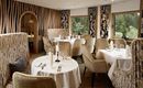An elegant restaurant with stylish seating and tasteful decoration. Large windows provide a view of the greenery.