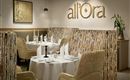 An elegant restaurant with modern dining areas and stylish furniture. The tables are elegantly decorated and there are plants to enhance the ambiance.