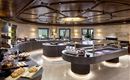 An elegant dining room with a round buffet and appealing lighting. On the tables, fresh pastries and various dishes are arranged.