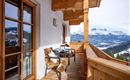 Een mooie balkon met houten bekleding en twee gezellige stoelen. Op de achtergrond zijn besneeuwde bergen en een heldere lucht te zien.