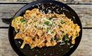 Een bord met pasta en een romige saus, gegarneerd met verse Parmezaanse kaas en peterselie. De pasta is op een zwart bord geserveerd en staat op een rustieke houten ondergrond.
