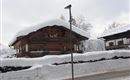 Ein traditionelles Holzhaus mit einem schneebedeckten Dach. Umgeben von Winterlandschaft und frischem Schnee.