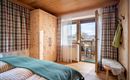 A cozy bedroom with a wooden ceiling and checked curtains. The balcony offers a view of the surroundings and fresh air.