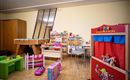A colorful play area with various toys, including a puppet theater and a pool table. The walls are bright, and the room feels welcoming for children.