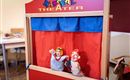 A puppet theater with colorful puppets is on a table. The puppets depict a Kasper and a girl who are waiting for a performance.