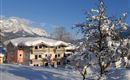 Ein gemütliches Haus im Schnee mit einem strahlend blauen Himmel. Die Umgebung ist von schneebedeckten Bergen und Bäumen geprägt.