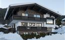 An impressive chalet in the Alps, surrounded by snow. The building has a traditional wooden style with balconies and large windows.
