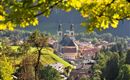 Ein malerisches Dorf in einer grünen Umgebung mit einer Kirche im Vordergrund. Die sanften Hügel und Bäume verleihen der Szene eine ruhige Atmosphäre.