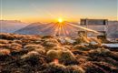 A beautiful sunrise over the mountains. A wooden bench stands in the foreground on the grass.