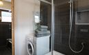 Een moderne badkamer met een douche en een wasmachine. Stapels grijze handdoeken liggen op de wasmachine.