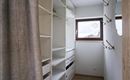 Een moderne ruimte met witte planken en een raam. Aan de muur zijn enkele haken voor kleding bevestigd.