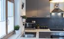 Een moderne keuken met grijze kasten en een RVS spoelbak. De ruimte is licht en smaakvol ingericht, met planten en een groot raam.