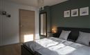 Een moderne slaapkamer met een groot bed, een spiegel en stijlvolle kunstwerken aan de muur. De kamer heeft een warme sfeer door de zonnestralen die naar binnen vallen.