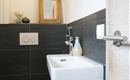 Een moderne badkamer met een stijlvolle wc en een klein wastafel. De muren zijn in een donkere tint gehouden en er zijn decoratieve elementen zoals een spiegel en een fles.