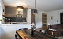 Een moderne keuken met een grote eettafel en een gezellig bank. De ruimte is licht en vriendelijk ingericht.